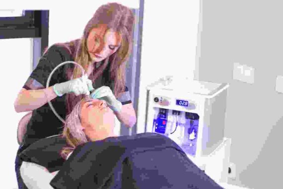 A woman is using an electric device to treat a man 's face.