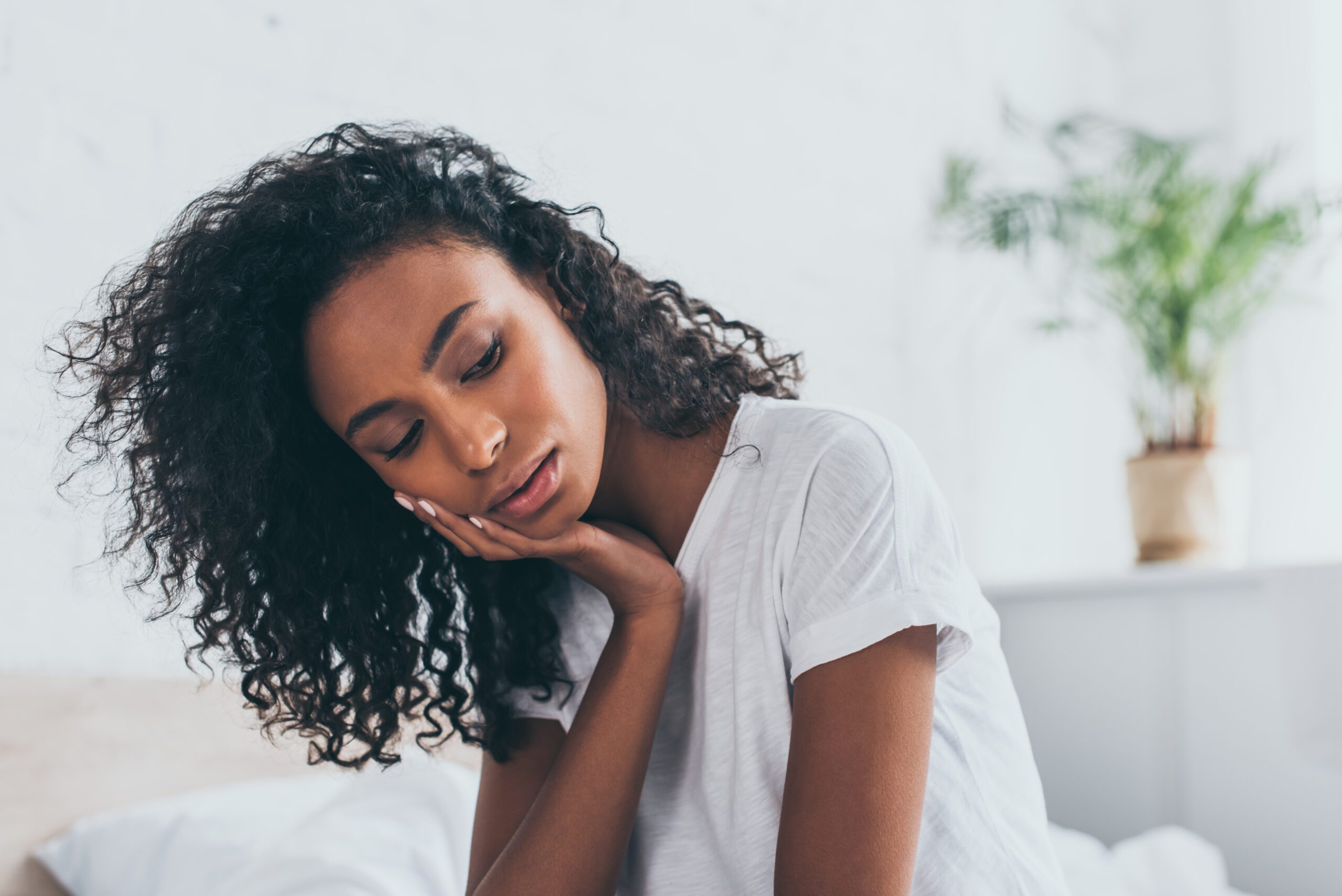 A woman sitting on top of her bed with her hand under her chin.
