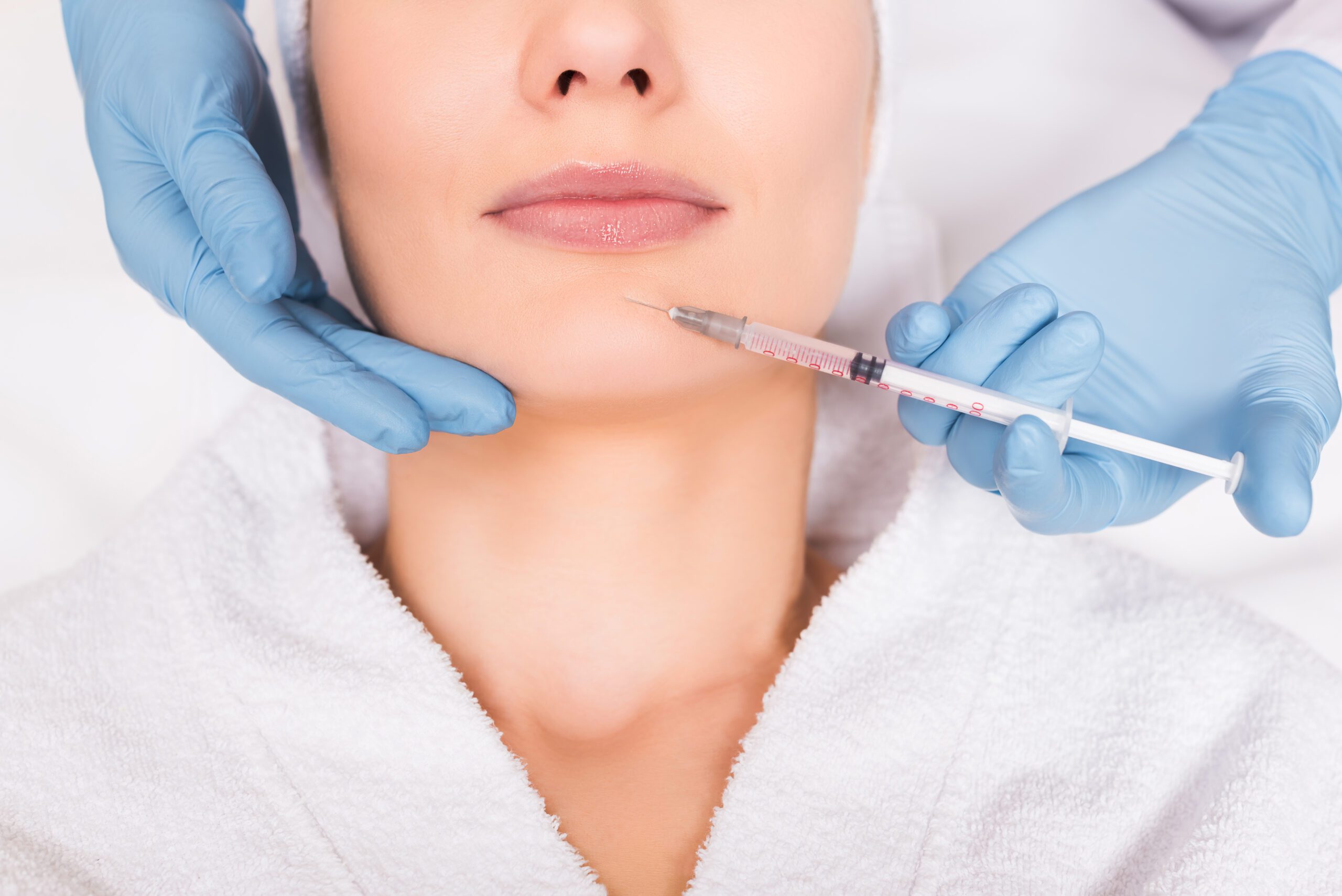cropped view of beautician injecting face woman at beauty salon A woman getting her lips waxed by an esthetician.