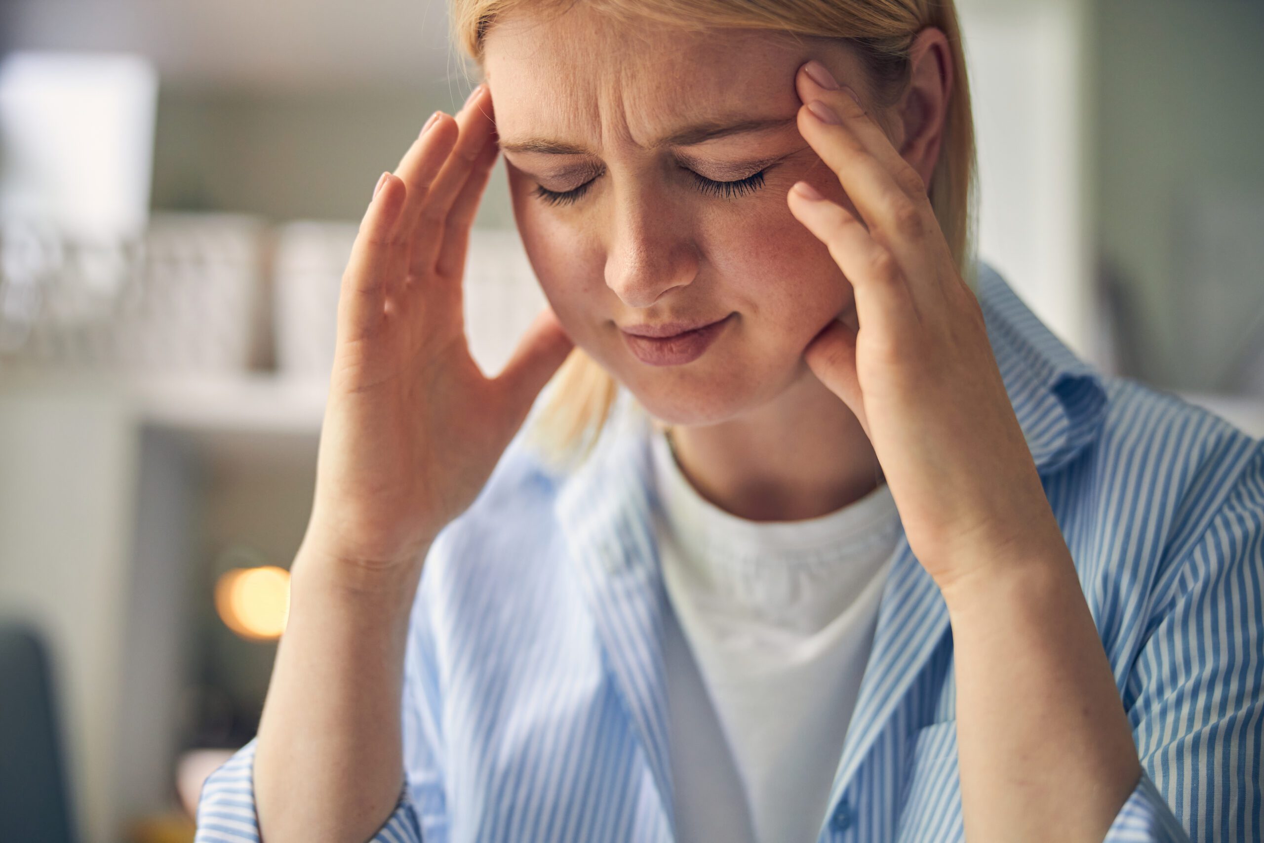Overworked blonde woman feeling pain in head A woman holding her head in pain with both hands.